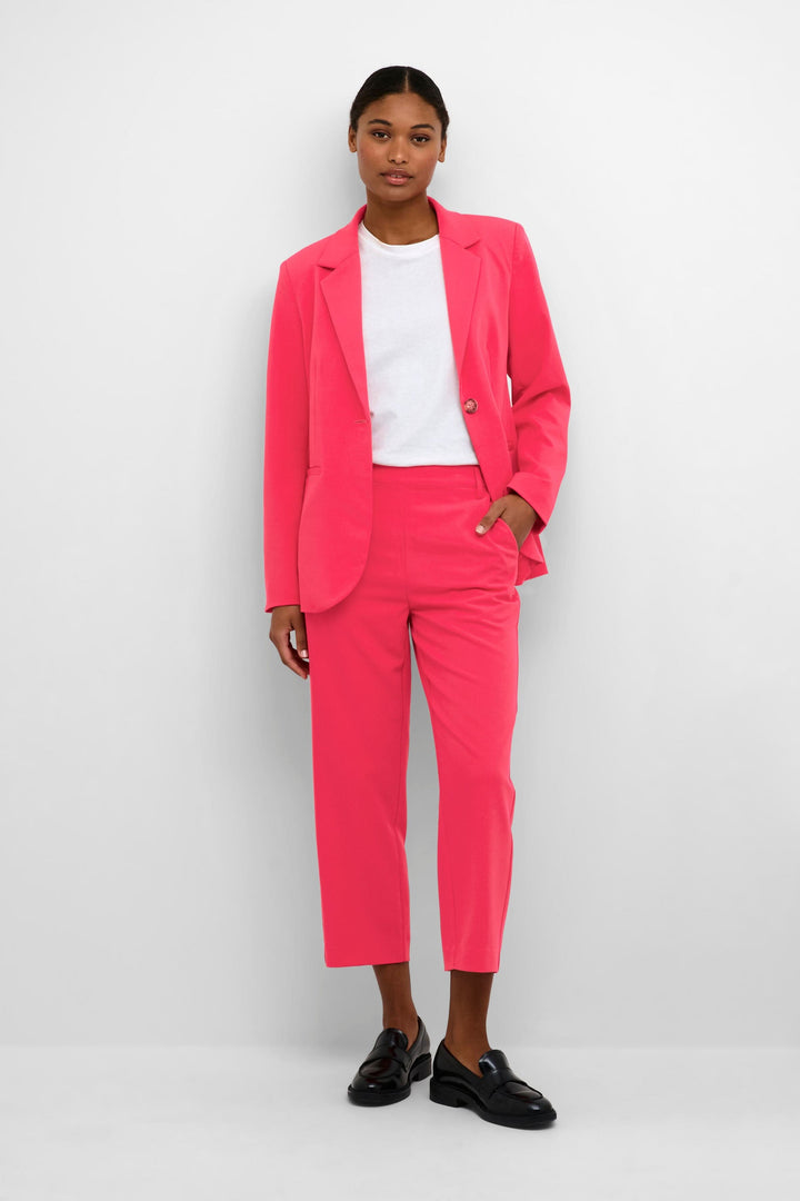 Femme en costume rose vif, pantalon court et blazer, disponible pour un style professionnel moderne.