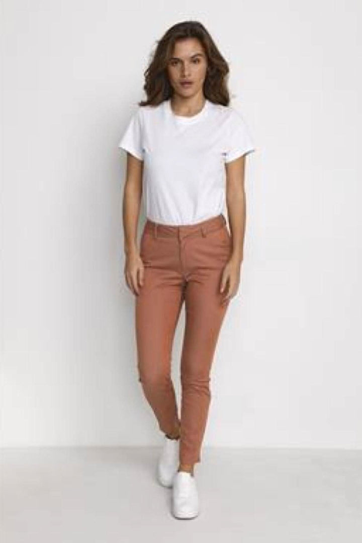 Femme portant un pantalon chino rose avec un haut blanc et des chaussures blanches, parfait pour l&