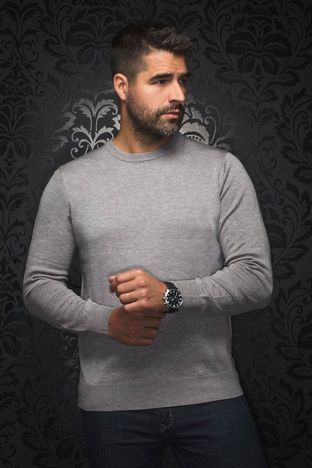 Homme portant un chandail col rond en mérinos gris pâle, avec arrière-plan orné.