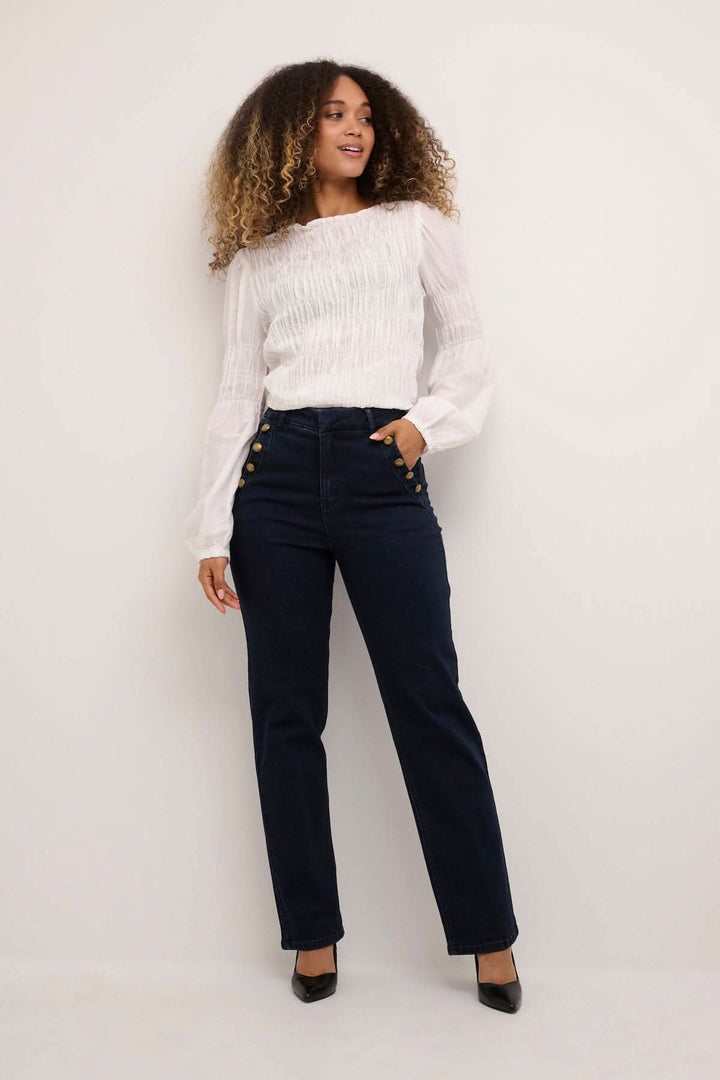 Femme souriante portant un jean noir ajusté avec 4 poches et boutons, associé à un haut blanc élégant.