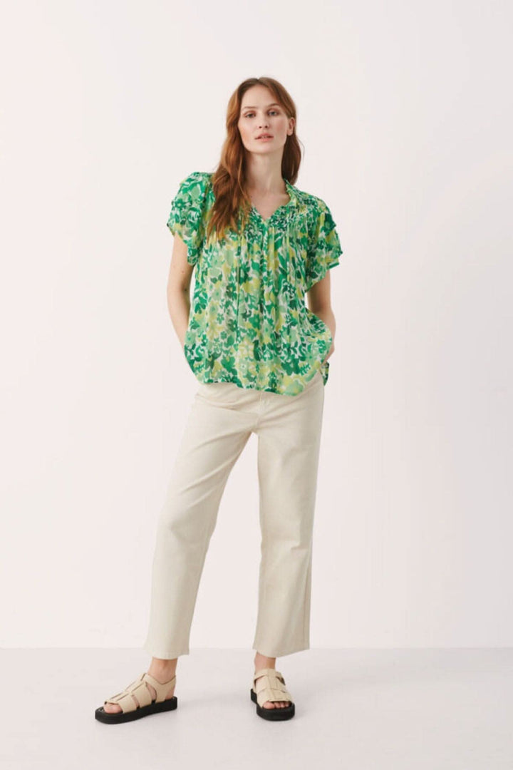 Blouse fleurie Sinna, légère et fluide, portée avec un pantalon crème, affichant un joli imprimé vert.