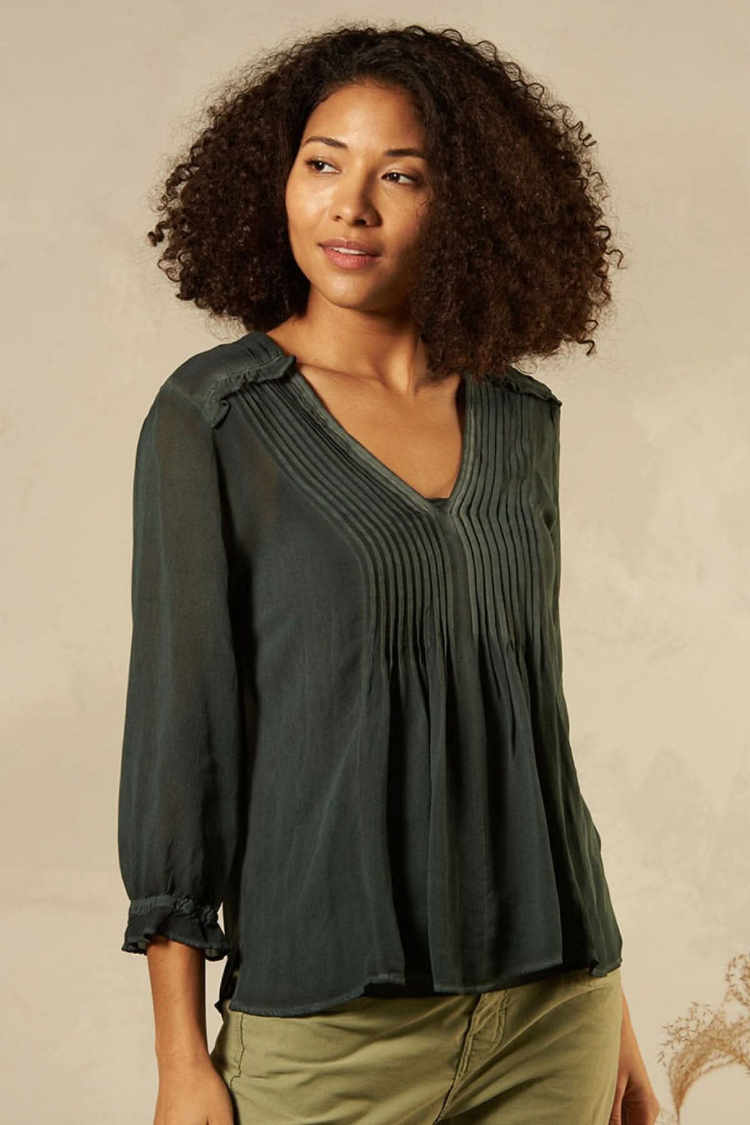 Blouse décontractée col en V, avec détails de couture, style moderne, portée par un modèle avec cheveux bouclés.