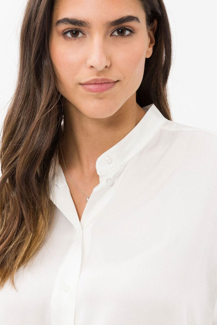 Femme portant une blouse soyeuse blanche sans col, avec des détails élégants et une finition chic.