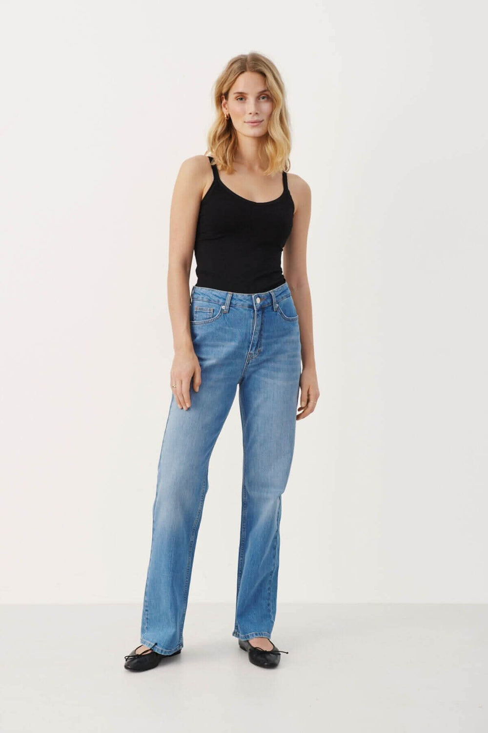 Femme portant un camisole noir à bretelles avec un col en V et un jean bleu décontracté, style moderne.