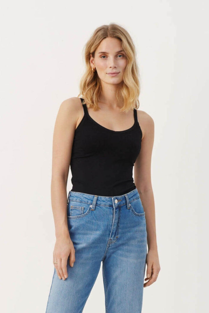 Camisole noire Hydda à bretelles minces et col en V, portée avec un jean classique.