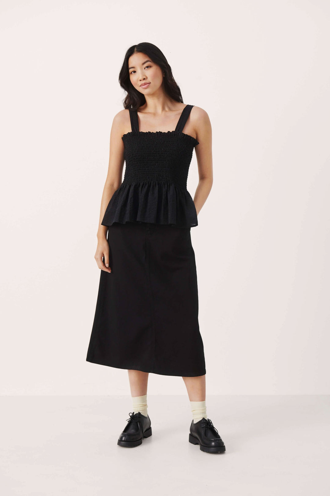 Camisole Stevie en noir avec bretelles larges et bas volant, associée à une jupe noire.