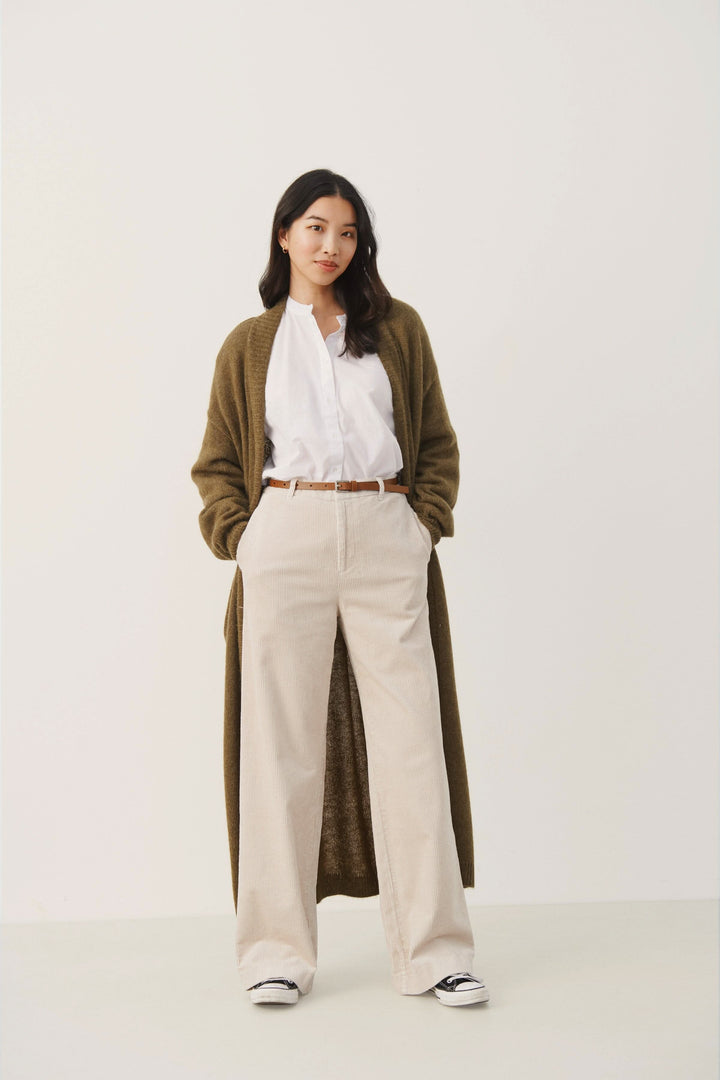 Femme portant une ceinture en cuir avec un pantalon beige et un cardigan vert, style décontracté.