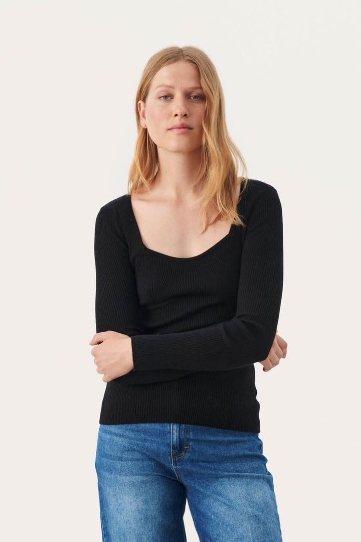 Chandail Caylee noir en tricot côtelé avec encolure profonde et longues manches, porté avec un jean.
