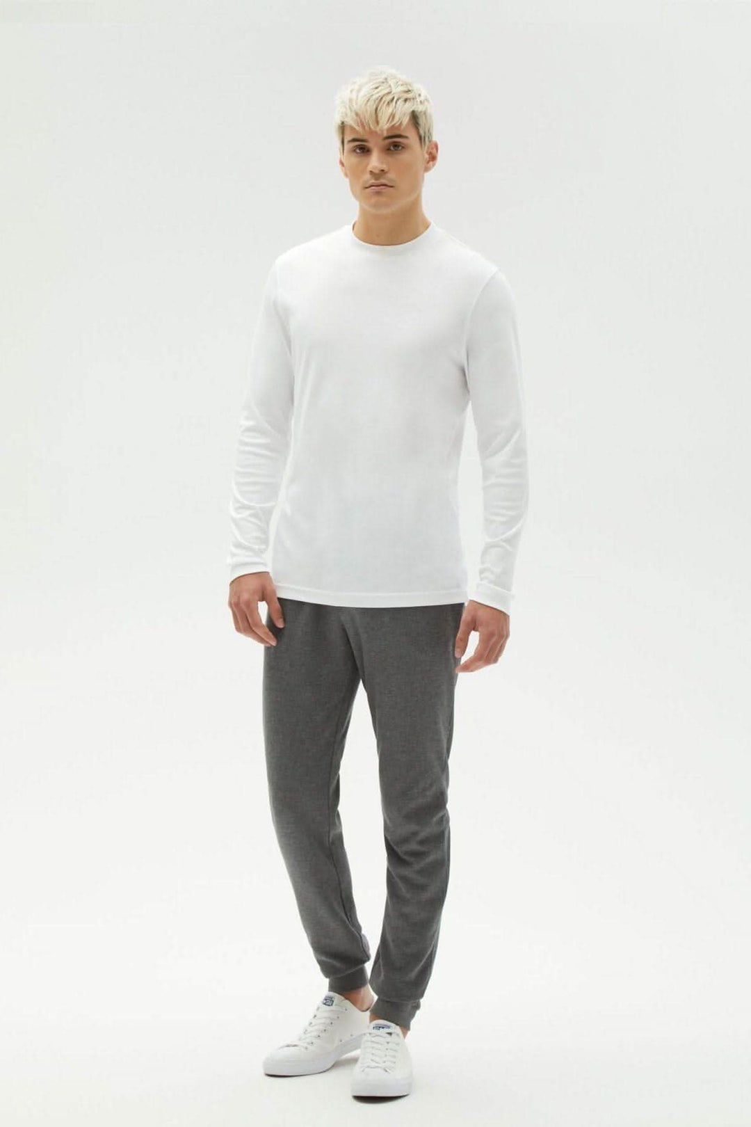 Modèle masculin portant un chandail manches longues blanc et pantalon gris, affichant un style décontracté et confortable.