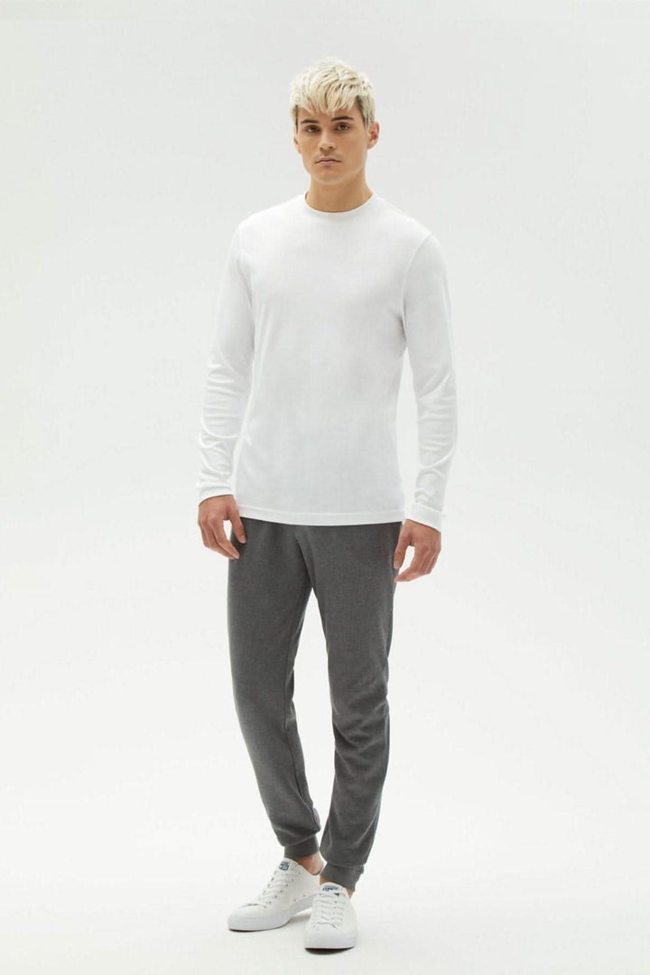 Modèle masculin portant un chandail manches longues blanc et pantalon gris, affichant un style décontracté et confortable.