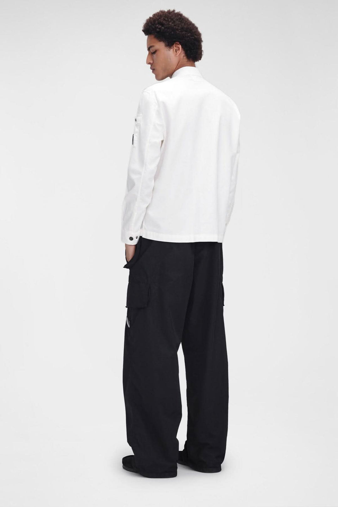 Homme de dos portant une chemise blanche à manches longues et un pantalon cargo noir.