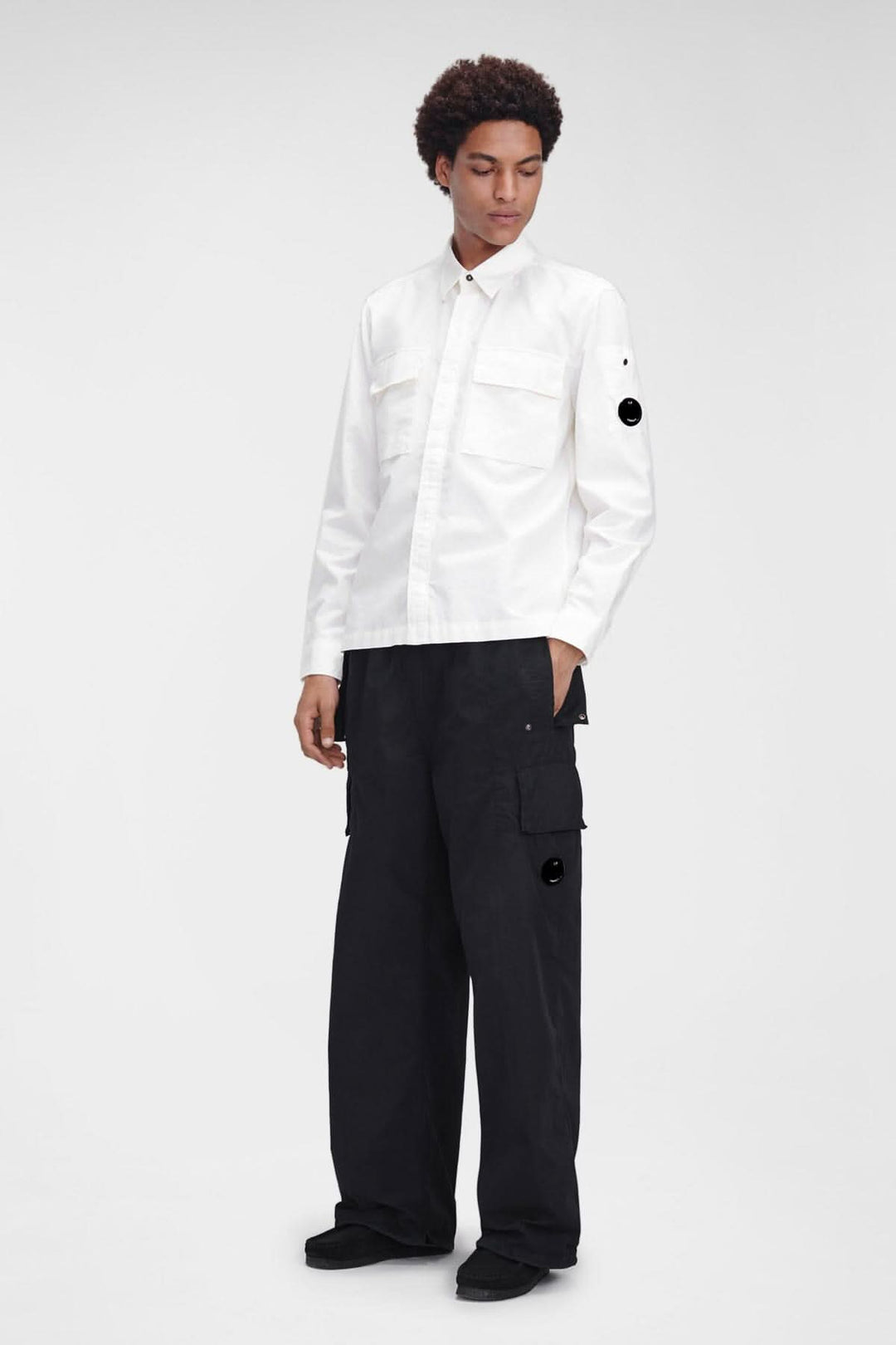 Homme portant une chemise blanche à manches longues et un pantalon cargo noir, mettant en valeur un style décontracté.