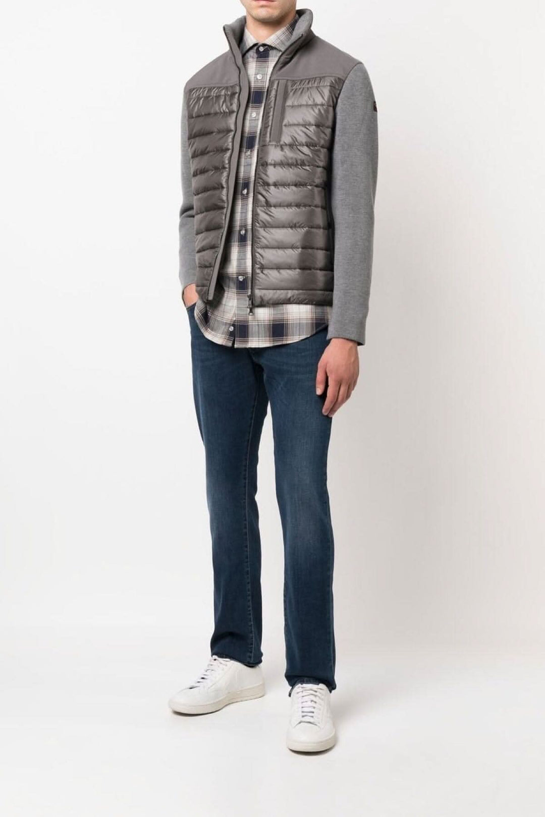 Homme en chemise à carreaux bleue et grise, sous un gilet matelassé, avec jeans et baskets blanches.