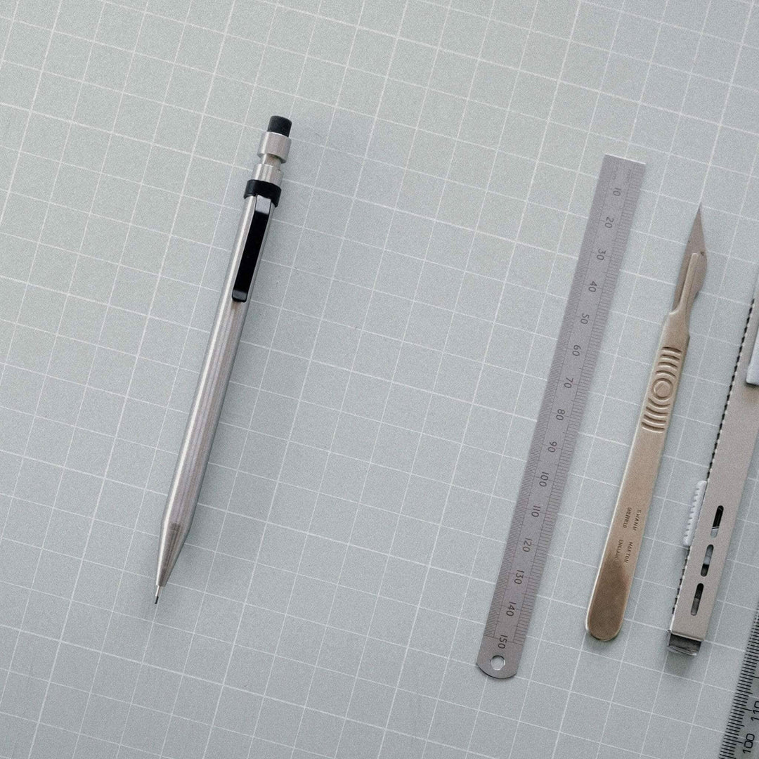 Crayon Modern Fuel en métal solide avec règle et outils sur fond de papier quadrillé.