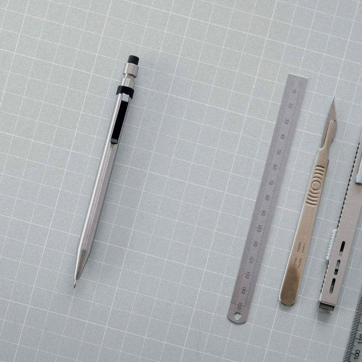 Crayon Modern Fuel en métal solide, avec règle, scalpels et autres outils de précision sur fond gris.