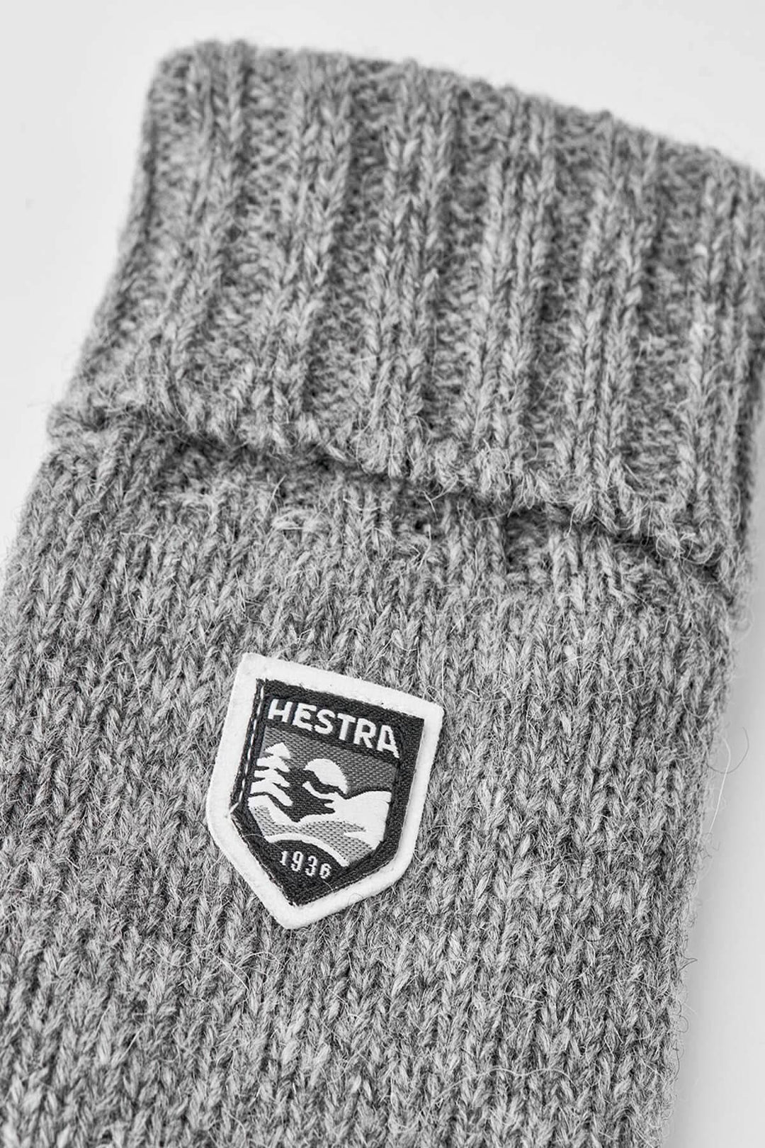 Gant en laine gris avec logo Hestra, texture tricotée et finition côtelée, parfait pour l&