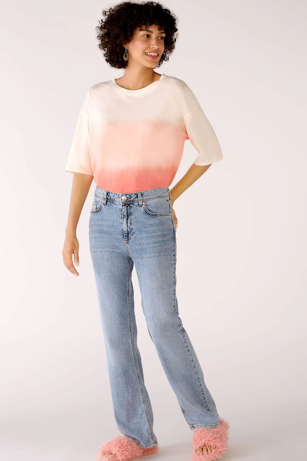 Femme portant un jean taille haute à jambe droite, t-shirt dégradé et chaussons en fourrure rose.
