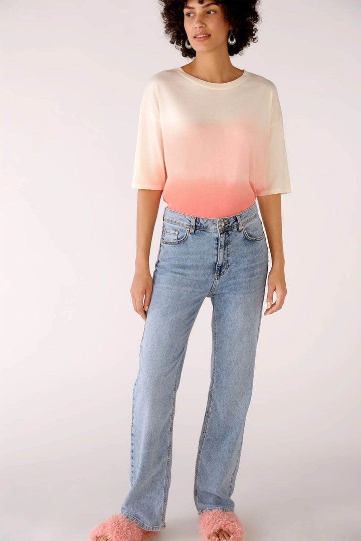 Femme portant un jean à taille haute et un haut dégradé, avec des chaussures confortables et une coiffure bouclée.
