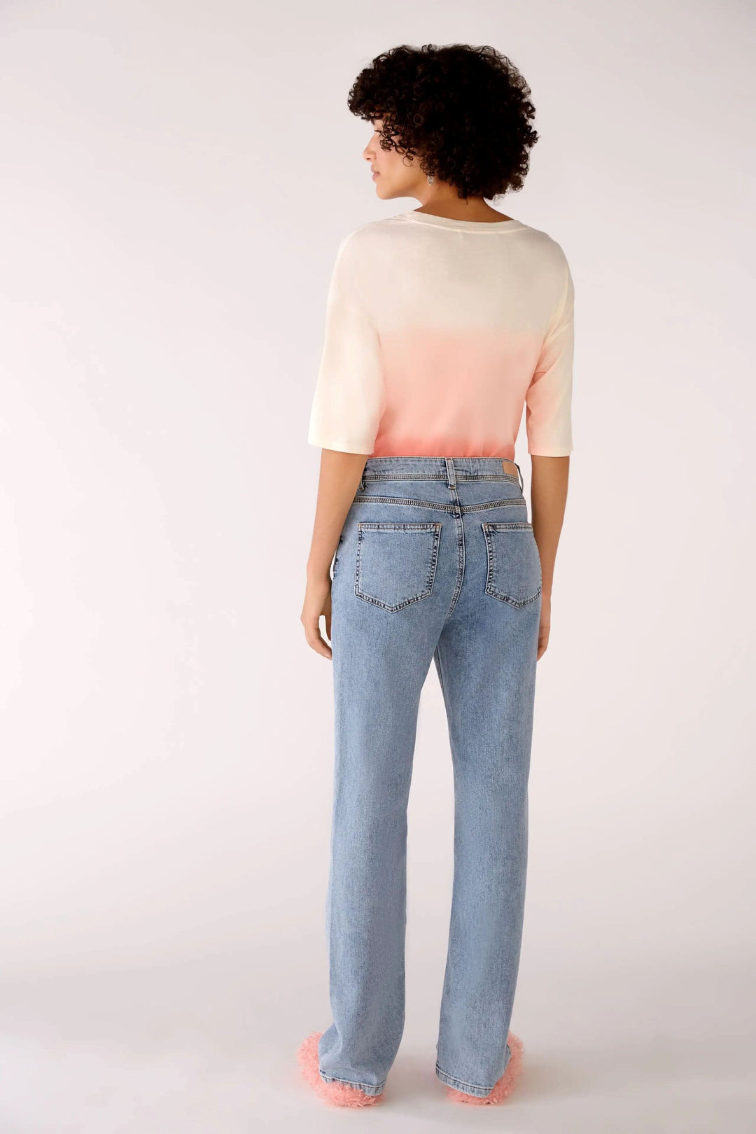 Femme vue de dos portant un jean taille haute avec une jambe droite et un haut dégradé rose et beige.