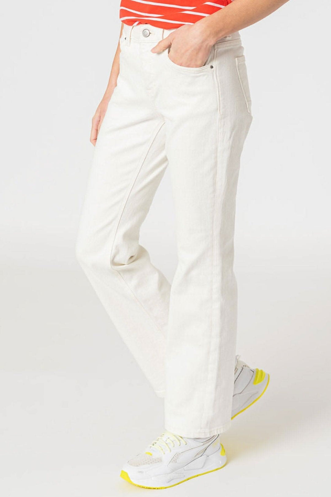 Jean bootcut blanc avec cinq poches et coupe ajustée, porté avec des baskets grises.
