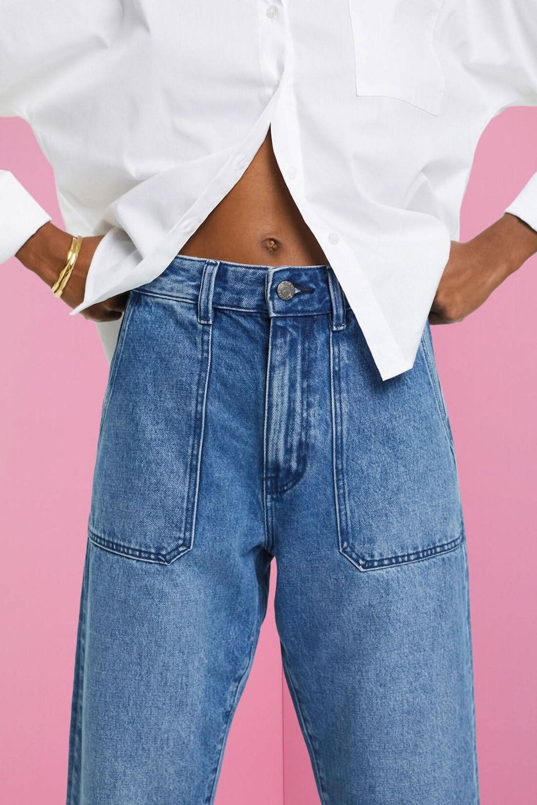 Jean coupe Dad avec poches avant et arrière, porté avec une chemise oversize blanche sur fond rose.