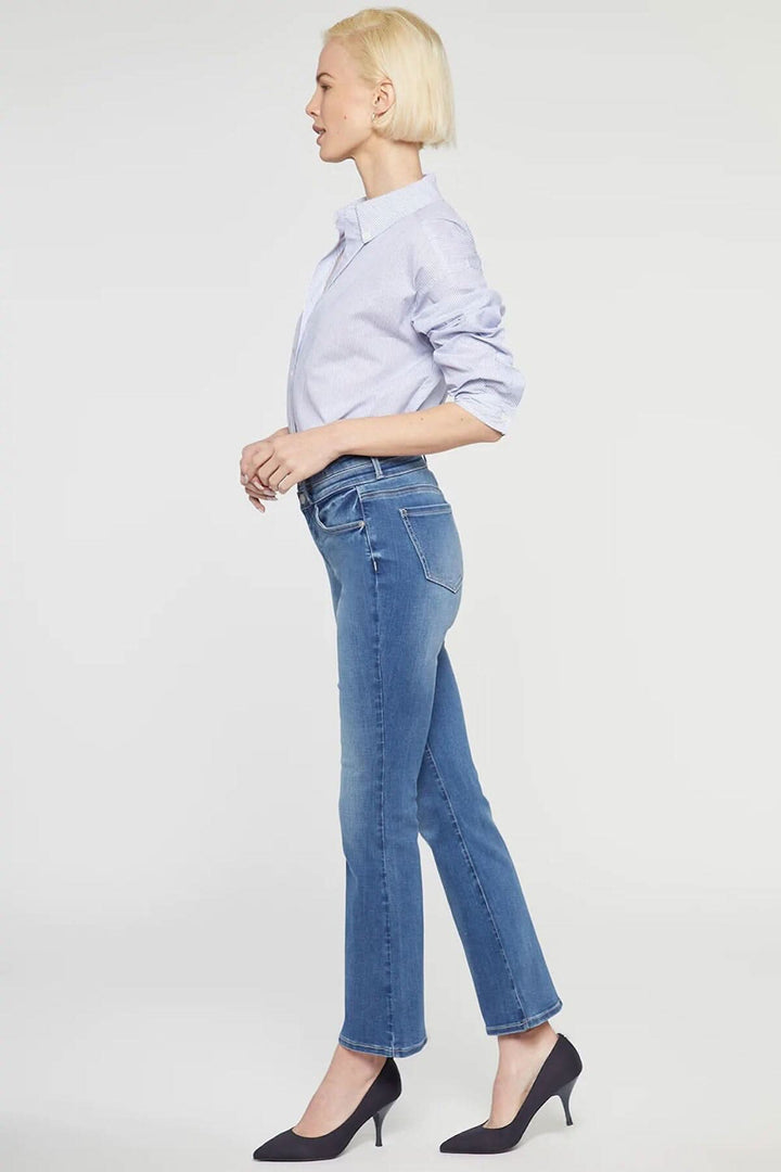 Jean évasé Ava de NYDJ, taille haute, silhouette tendance, porté avec une chemise bleu clair et des escarpins noirs.
