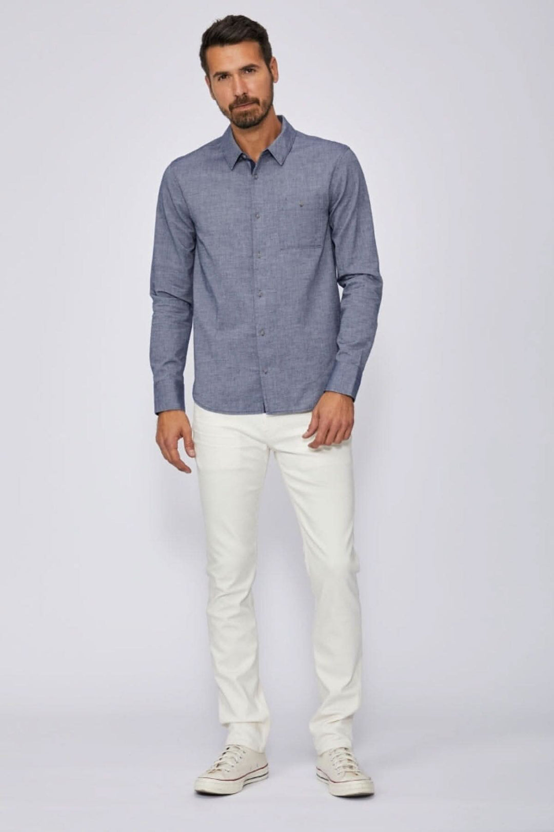 Homme portant une chemise bleue et un jean blanc cassé, look moderne et élégant.