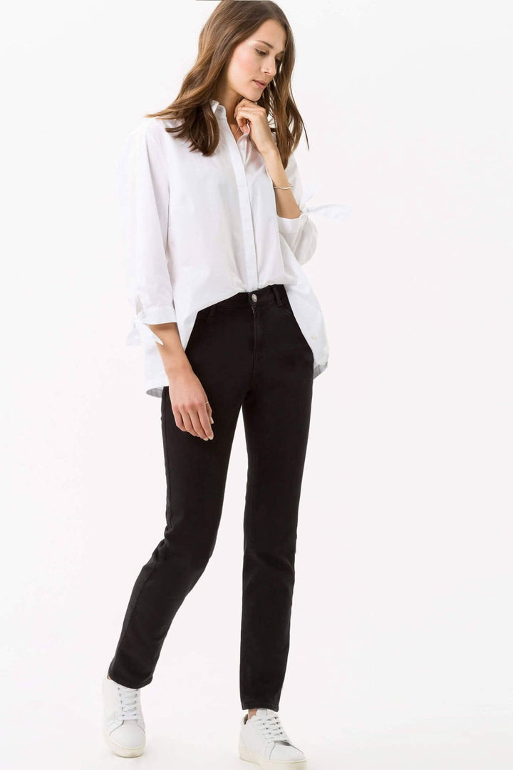 Femme portant le jean Mary de BRAX, coupe décontractée, avec chemise blanche et baskets blanches.