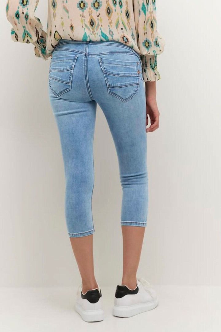 Femme portant un jean en coton bleu clair, vue arrière, associé à un top coloré et des baskets blanches.