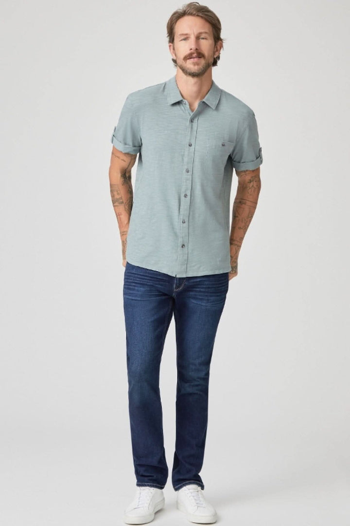 Homme portant une chemise à manches courtes verte et un jean foncé, styling décontracté.