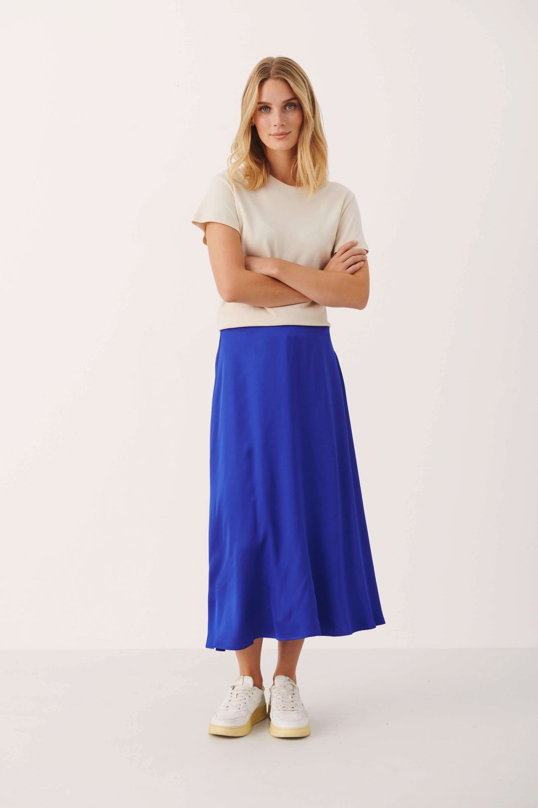 Modèle portant une jupe longue bleue en viscose, associée à un t-shirt beige, avec des chaussures blanches.