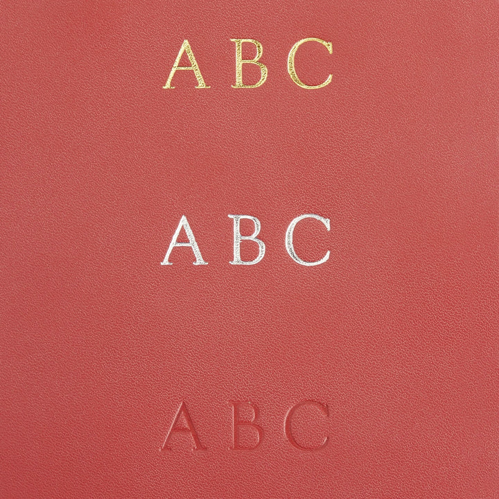Close-up of a leather surface featuring three monogram styles: gold, silver, and embossed letters &