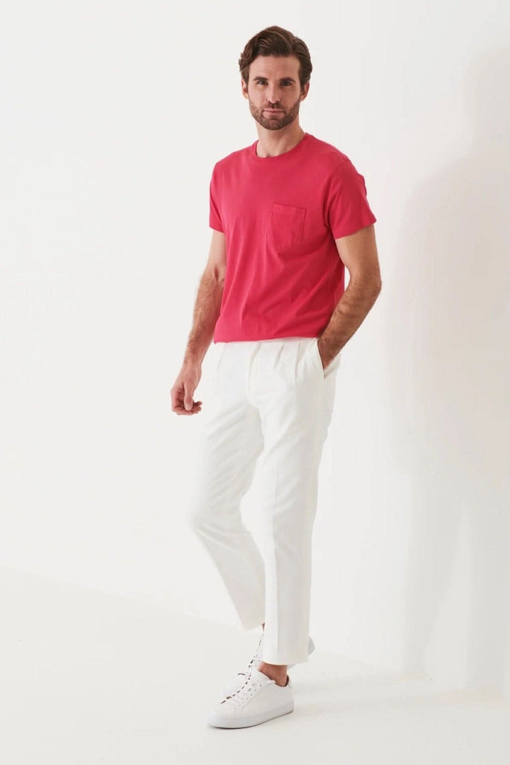 Homme portant un t-shirt léger en coton pima rose avec poche, associé à un pantalon blanc.