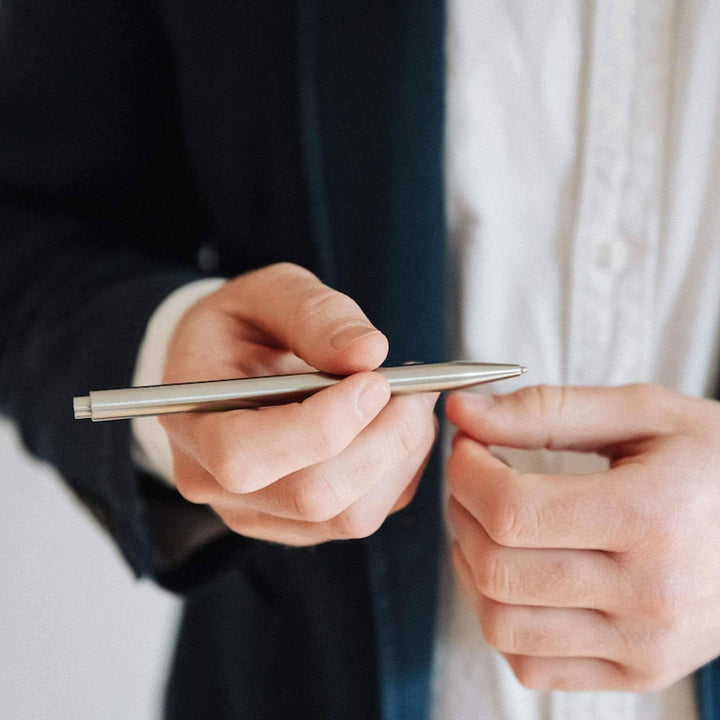 Stylo moderne Fuel en acier inoxydable, tenu par une personne en costume, idéal pour un style professionnel.