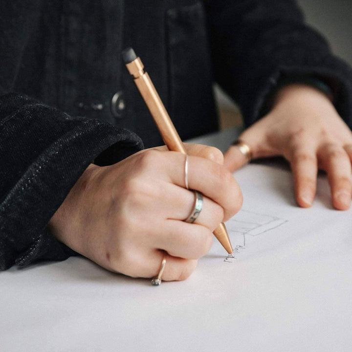 Mainly a hand holding a Modern Fuel crayon, sketching on a blank sheet of paper.