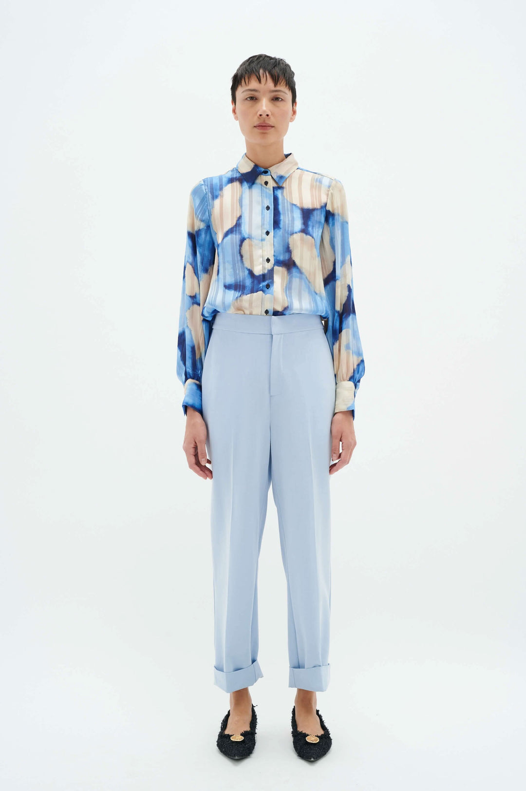 Femme portant une chemise à motifs colorés et un pantalon bleu clair à revers, sur fond blanc.
