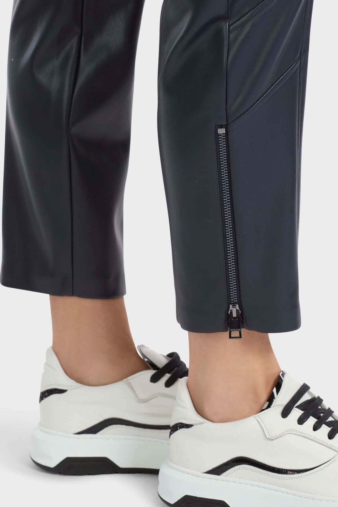 Pantalon en cuir noir SOFIA avec ourlet fendu et fermeture éclair, porté avec des baskets blanches.