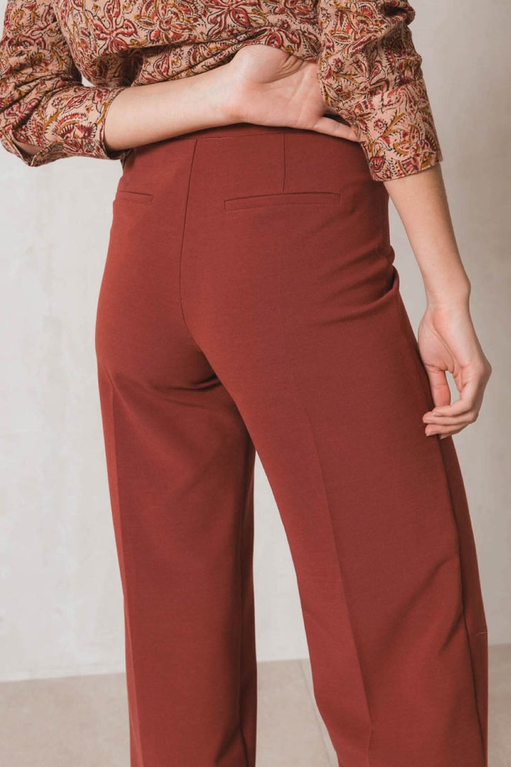 Pantalon habillé ample en rouge avec deux fausses poches et taille haute, porté avec une blouse imprimée.