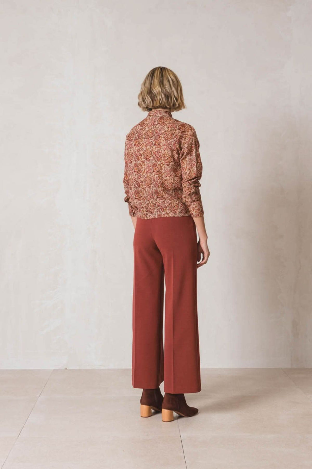 Femme de dos portant un pantalon habillé ample rouge et un pull à motifs floraux.