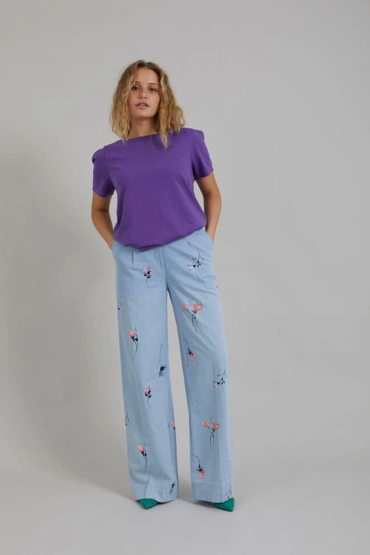 Femme portant un pantalon large en denim floral avec un haut violet, affichant un style décontracté et original.