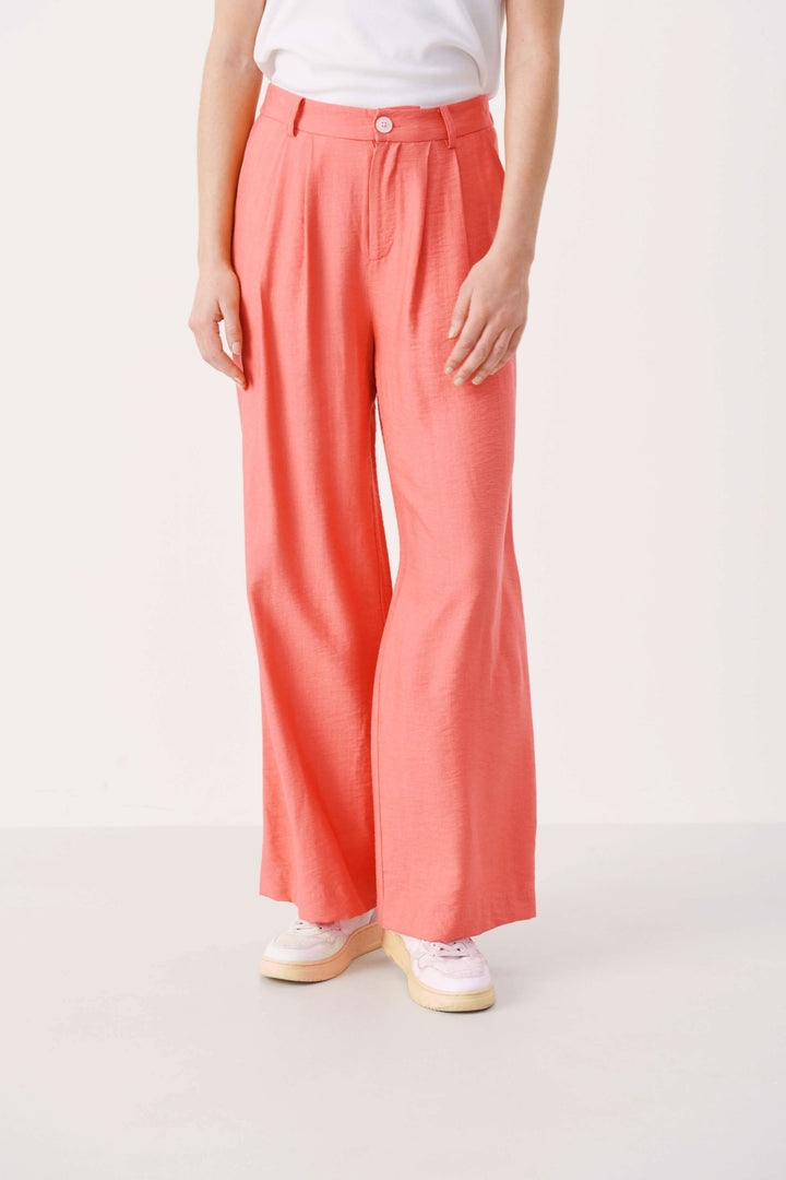 Pantalon habillé Sibille à jambe large en tissu fluide, couleur corail, avec ceinture et fermeture à bouton.