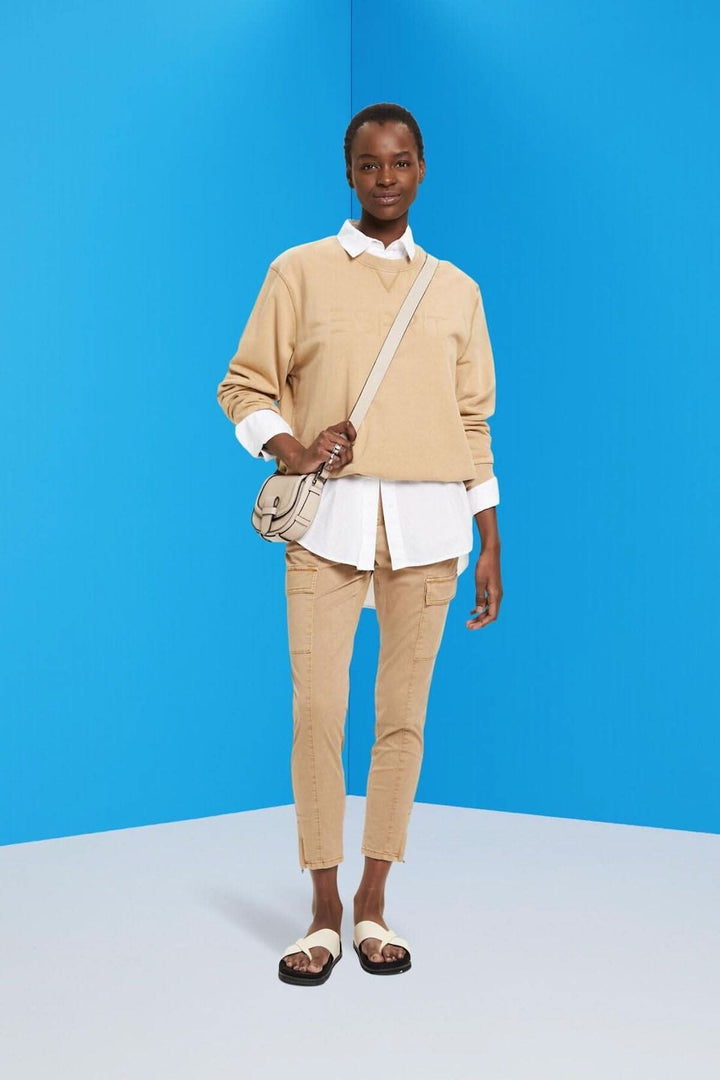 Femme portant un pull beige et un pantalon cargo mi-haut, avec un sac à main sur fond bleu.