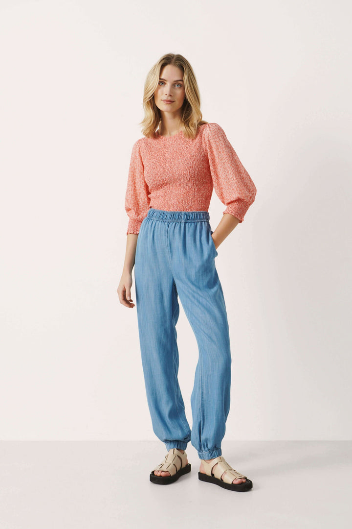 Femme portant un top rose et un pantalon décontracté en lyocell bleu, style jogging, avec poches.