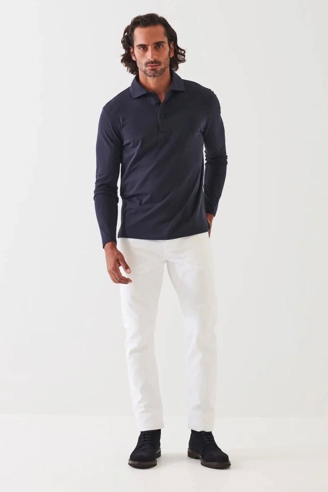 Homme portant un polo stretch en coton à manches longues, avec pantalon blanc et chaussures noires.