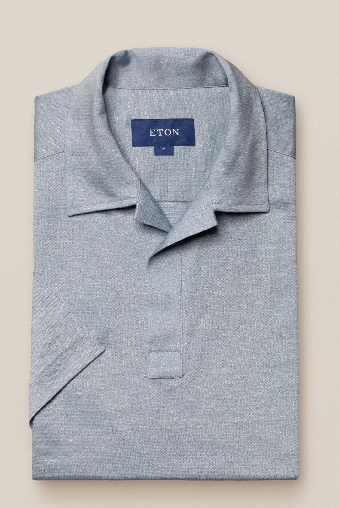 Polo en lin et coton de couleur grise, plié avec col ouvert, style moderne, étiquette ETON visible.