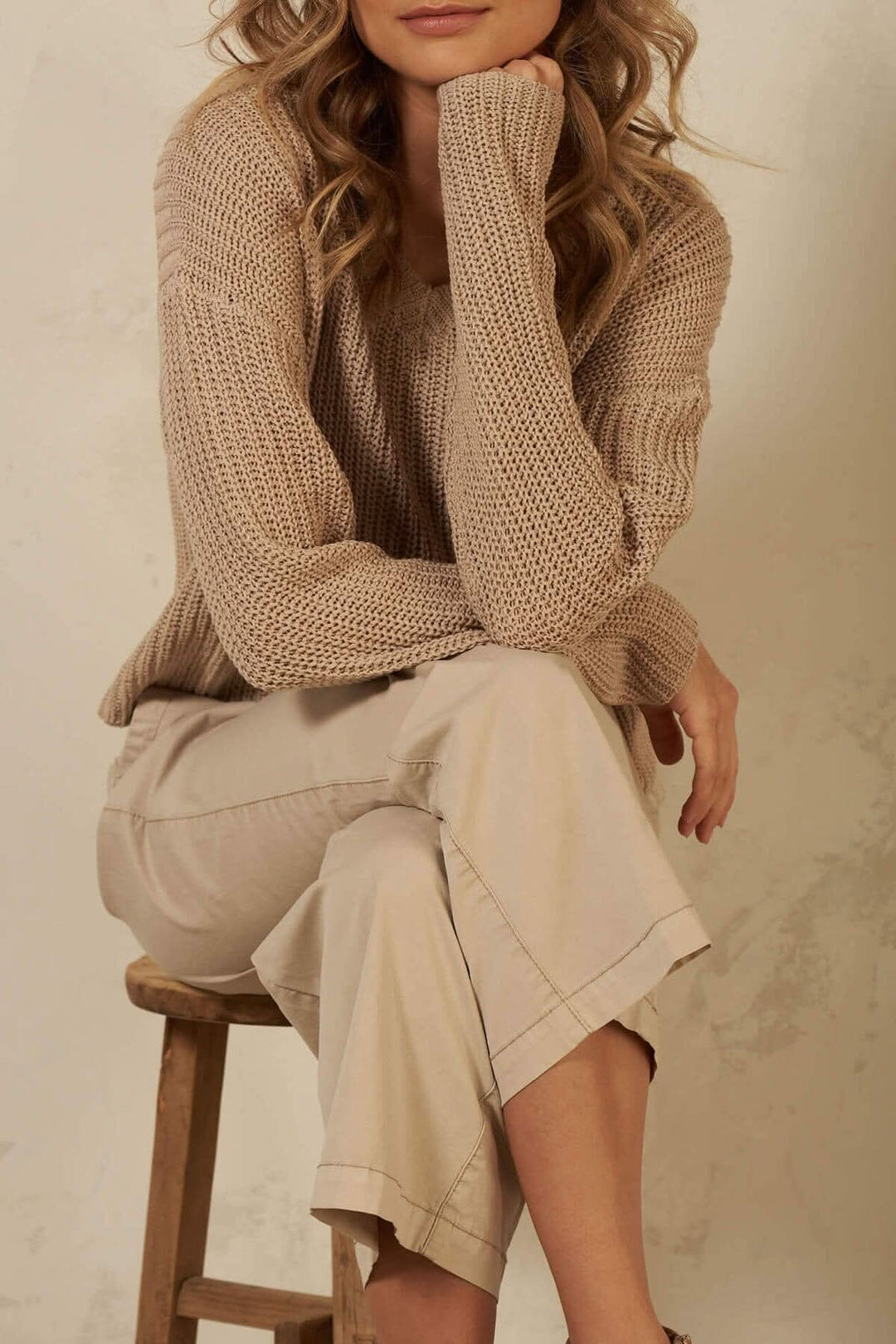 Pull à mailles en coton avec col en v, porté avec un pantalon léger, style décontracté et tendance.