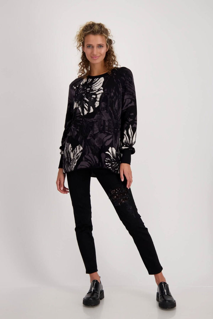 Pull en maille de coton à motif floral noir, coupe droite et volants aux manches, porté avec un pantalon noir.