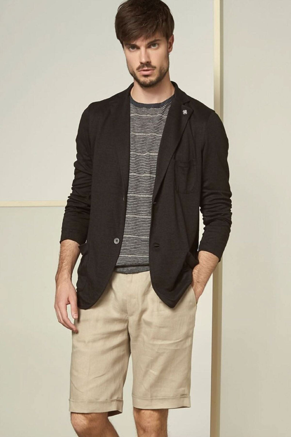 Homme portant un blazer noir avec un t-shirt à rayures et un short beige, look décontracté et stylé.