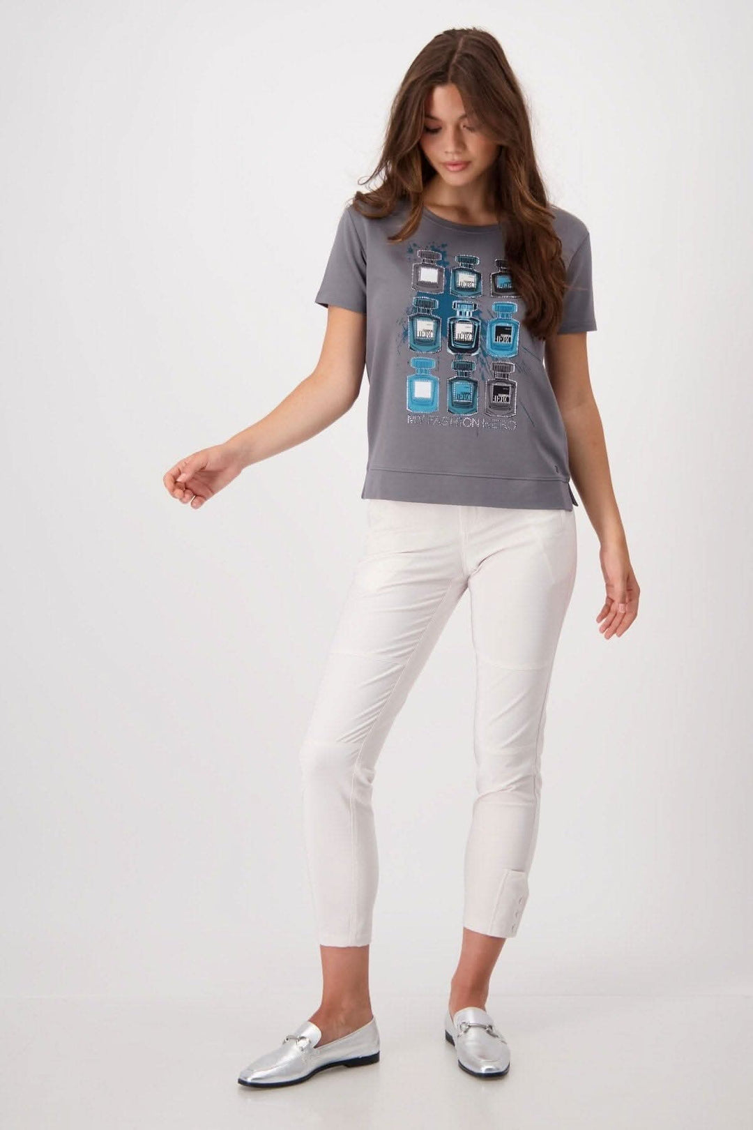 T-shirt grey with bottle print and rhinestones, paired with white pants and silver shoes on a model.