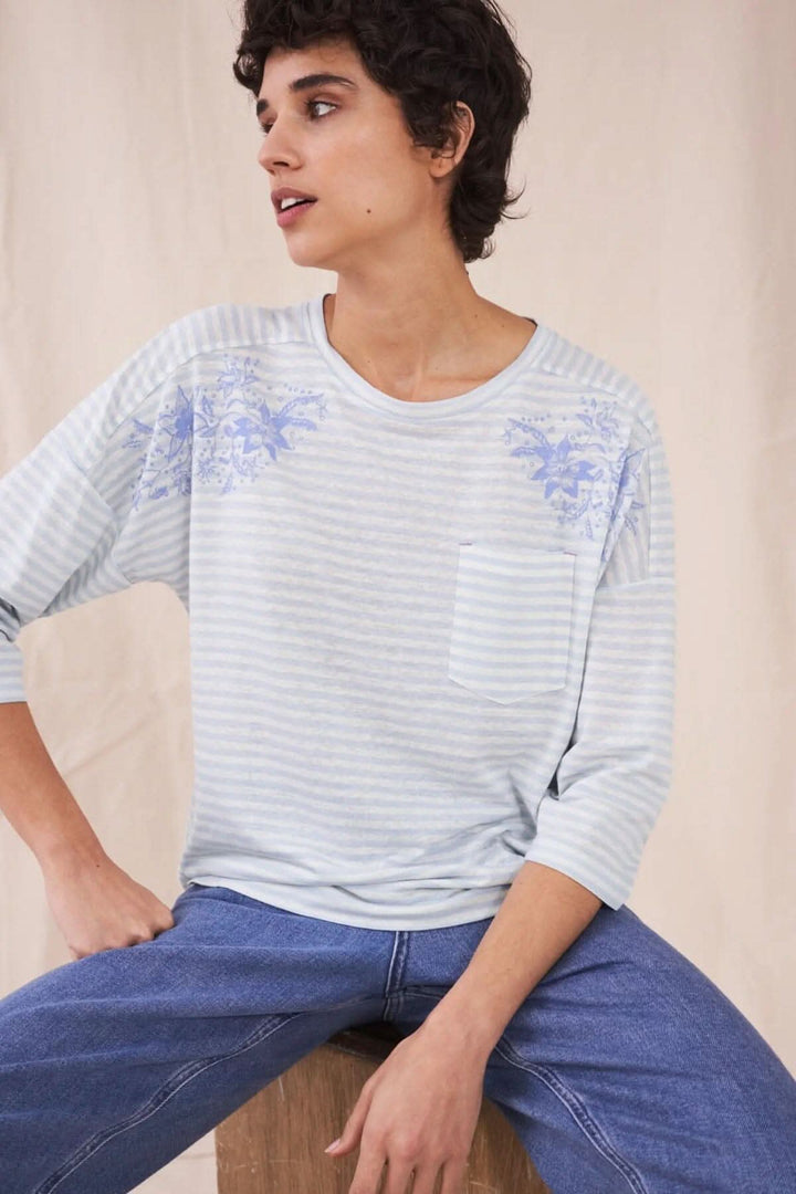 T-shirt Lennox à rayures bleues avec broderies, porté par une femme assise, jean décontracté.